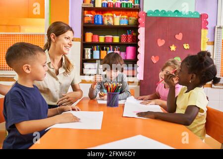 Educatore e gruppo di bambini in un corso di pittura creativa in un asilo internazionale o in un centro di assistenza post-scolastica Foto Stock