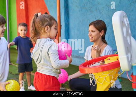 Insegnante di sport e bambini che giocano a palla in classe sportiva in assistenza diurna o prescolare Foto Stock