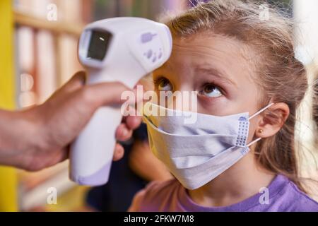 Bambino con maschera facciale durante la misurazione della febbre con termometro clinico a infrarossi senza contatto Foto Stock