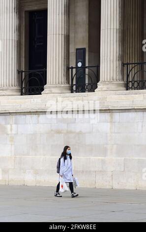 Londra, Inghilterra, Regno Unito. Lone Asian Woman con shopping in Trafalgar Square indossando un facemask durante il pandemice COVID, Aprile 2021 Foto Stock