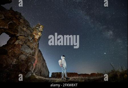 Spaceman in speciale tuta bianca e casco in piedi e guardando su cielo stellato con Via Lattea di notte. Concetto di astronomia e viaggio cosmico. Foto Stock