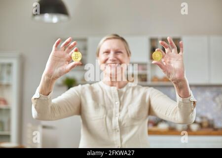 Una donna anziana tiene due monete di bitcoin nelle sue mani. Concetto di vita di pensione felice Foto Stock