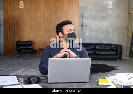 Ritratto di un uomo indiano preoccupato in maschera facciale protettiva sul posto di lavoro in ufficio, il dipendente maschile si è protetto dall'infezione virale durante il periodo pandemico, nuove regole e norme sociali Foto Stock