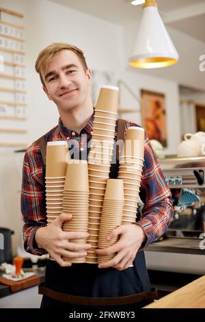 barista in grembiule che tiene un sacco di tazze di carta usa e getta Foto Stock