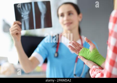 Il medico esamina i raggi X della mano accanto al paziente in piedi con mano bendata Foto Stock