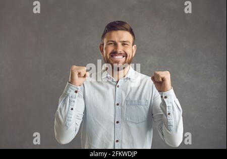 Uomo con gli occhi chiuso pugno clenching festeggiando successo in piedi studio scatto Foto Stock