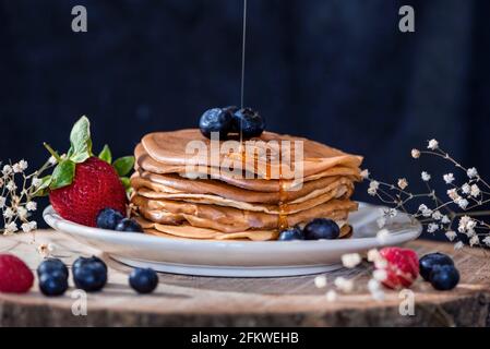 Deliziosi pancake fatti in casa con frutta di foresta e miele su un piatto di servizio in legno, primo piano, macro fotografia Foto Stock