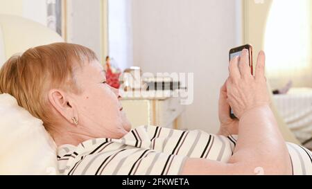 Una donna anziana si trova nella camera da letto con un telefono tra le mani. Foto Stock