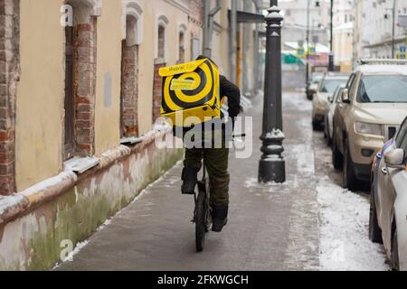 Città di Mosca, regione di Mosca, Russia 12.16.2020 Yandex corriere di cibo corre una bicicletta in fondo alla strada. Consegna a domicilio. Un uomo guida una bicicletta con un refr Foto Stock