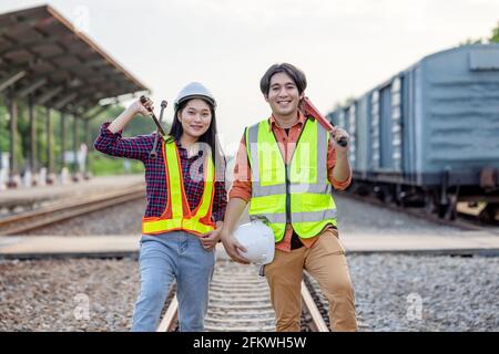 Il tecnico addetto alla manutenzione in un tuta di sicurezza si trova accanto a un treno merci con la chiave. I lavoratori asiatici lavorano nel settore dei trasporti ferroviari. Ingegnere Foto Stock