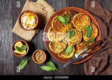 frittelle di spinaci di ceci su un piatto di argilla su un tavolo di legno scuro con hummus in una piccola ciotola, piatto Foto Stock