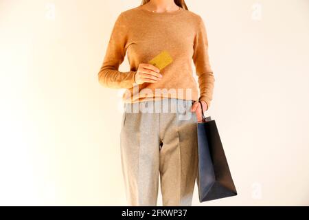 Giovane donna slim in classico outfit alla moda, pullover marrone e pantaloni grigio sciolto sono andati a fare shopping, tenendo borse di carta e vip Golden credito / debito auto Foto Stock