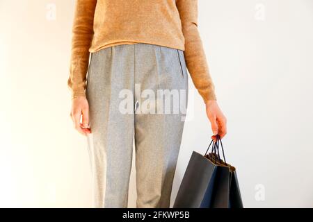 Giovane donna slim con abito classico alla moda, pullover marrone e pantaloni grigio sciolto, shopping, borse di carta. Sfondo bianco, spazio per la copia, chiudere Foto Stock