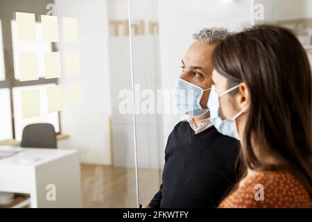 I colleghi di lavoro discutono di idee sulla lavagna di vetro in ufficio - concetto di business Foto Stock