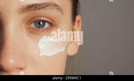 Giovane donna mette una crema bianca sul viso Foto Stock