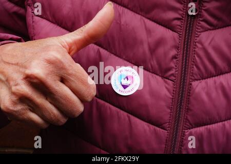 Badge adesivo "ho avuto la mia vaccinazione Covid" sulla giacca trapuntata di maroon, con i pollici di una donna adulta più anziana. Foto Stock