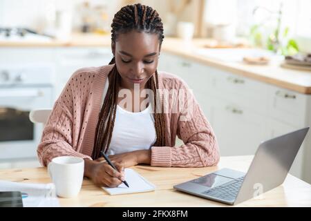 Studiare a casa. Giovane studentessa nera con laptop in cucina Foto Stock