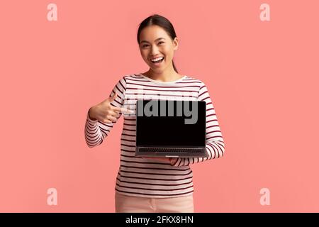 Happy Young Asian Woman punta al laptop con schermo nero Nelle mani Foto Stock