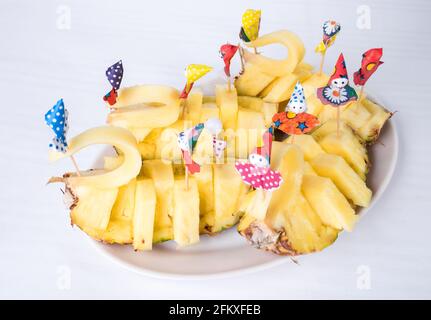 Delizioso ananas a fette con ombrelli di carta. Piatto situato su uno sfondo tovaglia di tela bianca. Foto Stock