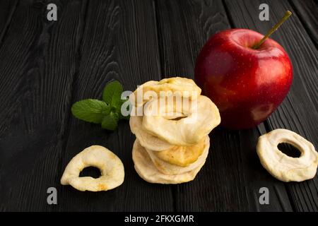 Chip di mela e mela rossa su sfondo di legno nero. Primo piano. Foto Stock