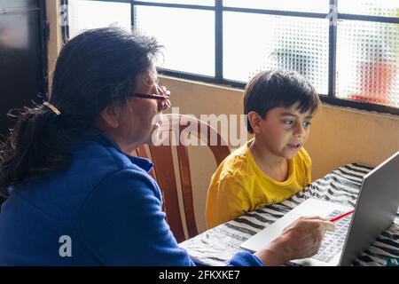 Nonna ispanica casa scolando nipote online, ragazzo ispanico bambino utilizzando notebook online istruzione Foto Stock