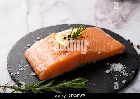 salmone crudo servito su un piatto di ardesia con limone e. rosmarino sul tavolo Foto Stock