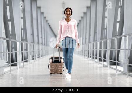 Viaggi aerei. Felice donna afroamericana a piedi nel terminal dell'aeroporto con valigia Foto Stock