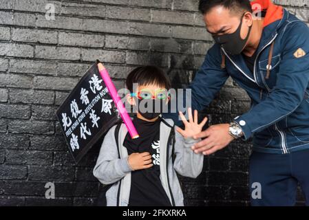 Hong Kong, Cina, 12 gennaio 2020, UN padre fa fare il suo bambino fare il segno 'cinque richieste' dopo averlo vestito come un protetore, durante un pro-democratico Foto Stock