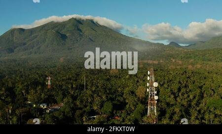 Antenne e microonde piatti di collegamento della rete di telefonia mobile e trasmettitore TV su torri di telecomunicazione con le montagne e la foresta pluviale. Camiguin, Filippine Foto Stock