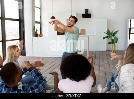 Gruppo di amici multirazziali felici che giocano charades indovinare gioco a. casa Foto Stock