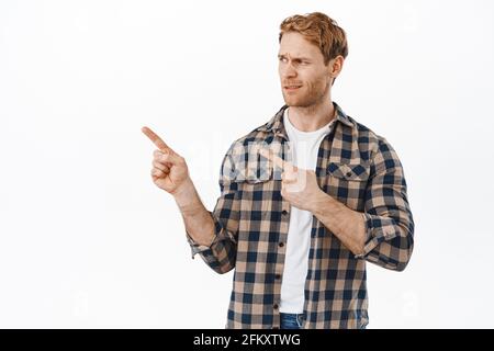 L'uomo adulto scettico e dispiaciuto con i capelli rossi, puntando e guardando a sinistra giudicante, accigliato come fissando qualcosa di ridicolo o stupido Foto Stock