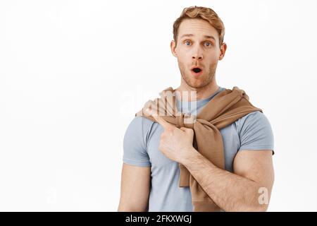 Bell'uomo rosso stupito che fa il gasting, dica il wow e che punta all'articolo in alto a sinistra dell'angolo, mostrando il logo o la bandiera del prodotto, impressionato dal testo promozionale Foto Stock