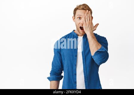 Immagine di rosso uomo coprire metà del viso con la mano, fissando stupito, gasping e caduta mascella dire WOW, guardando qualcosa di fantastico, in piedi sopra Foto Stock