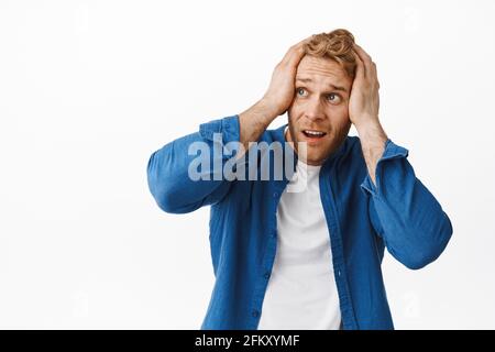 L'uomo rosso tormentato e ansioso copre la testa con le mani e guardando preoccupato a sinistra, ansimando, piegandosi come fissando allarmato di qualcosa di scioccante Foto Stock