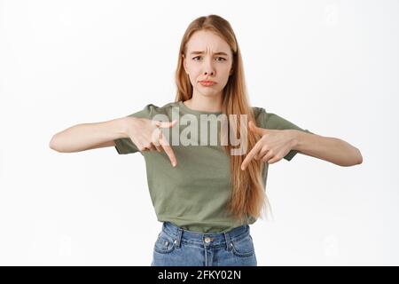 Ragazza triste e cupa che punta le dita verso il basso, sulking e accigliando a ingiusta situazione sconvolgendosi, lamentandosi, si sentono gelosi o delusi, in piedi Foto Stock