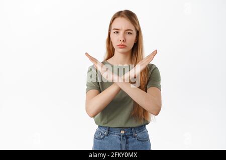Giovane studentessa mostra gesto cross stop, dire no, blocco e tabù gesto, in piedi dispiaciuto e vietare cattiva azione, sfondo bianco Foto Stock