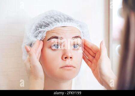 Un makeup master permanente che controlla la simmetria delle marcature delle sopracciglia prima della procedura. Foto Stock