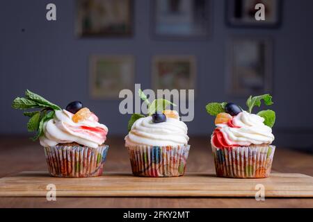 tre cupcakes di crema su un asse di legno Foto Stock