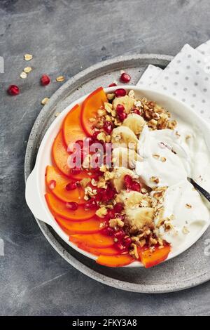 Yogurt con persimmon, banane, avena e noci su sfondo grigio. Foto Stock