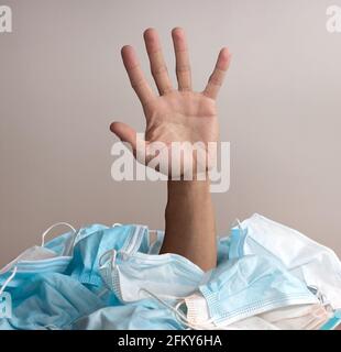 Problemi di salute mentale durante covid-19 o concetto di inquinamento dei maks facciali di igiene. Mano che emerge dal mucchio di maschere Foto Stock