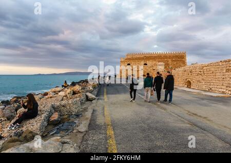 Heraklion, Creta, Grecia. La fortezza di Koules (castello a mare) al vecchio porto veneziano. Persone che camminano e si rilassano sulle acque frangiflutti al tramonto Foto Stock