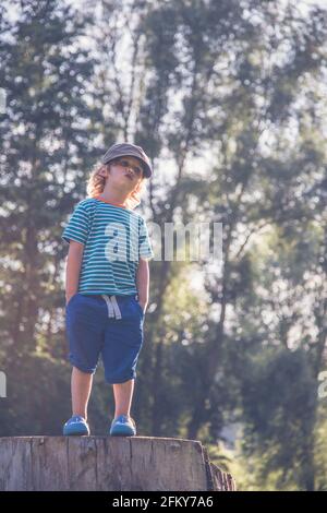 Young Boy si trovava su un tronco d'albero facendo espressioni diverse Foto Stock