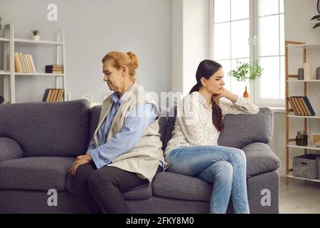 La donna anziana offesa e la figlia adulta sono sedute sul divano con le spalle l'una all'altra. Foto Stock