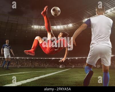 L'attaccante di calcio in uniforme rossa colpisce il pallone con un calcio acrobatico in aria allo stadio Foto Stock