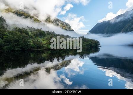Una nuova mattina che si innamora a Doutful Sound, nuvole che pendono in basso nelle montagne, Isola del Sud della Nuova Zelanda Foto Stock