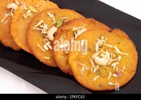 Accatastato delizia indiana Mawa Malpua Mithai beve in Cheeni Ki Chashni o Chaashni e disposti su vassoio nero decorato con Frutta secca Pistachios Pi Foto Stock