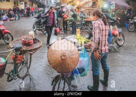 Hanoi, Vietnam - Febbraio 28 2019: Un venditore locale di strada vietnamita vende frutta dal retro della sua bicicletta in una giornata piovosa nella vivace città stree Foto Stock