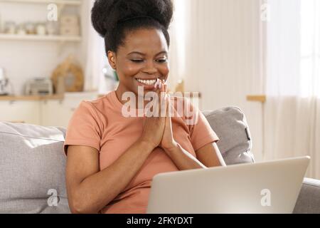 Donna nera molto gioiosa guardare il laptop più allegro per le buone notizie, ragazza africana leggere e-mail o messaggio sul divano Foto Stock
