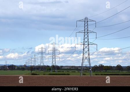 Tralicci elettrici ad alta tensione della rete nazionale che attraversano terreni agricoli parzialmente arati nel Nord Yorkshire, Regno Unito Foto Stock