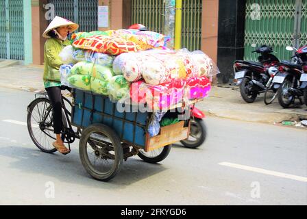 Commerciante con cappello conico che trasporta grande carico di arredamento morbido sul rickshaw del ciclo, ho Chi Minh City, Vietnam, Asia Foto Stock